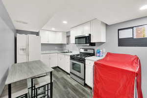 Kitchen with appliances with stainless steel finishes, white cabinetry, dark wood-type flooring, and sink