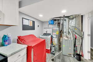 Clothes washing area with cabinets, washing machine and dryer, light hardwood / wood-style floors, and water heater