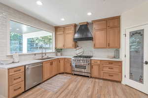 Kitchen with sink, stainless steel appliances, backsplash, custom range hood, and light wood-type flooring