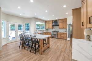 Kitchen featuring a kitchen bar, appliances with stainless steel finishes, french doors, custom exhaust hood, and light hardwood / wood-style flooring