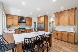 Kitchen featuring backsplash, a kitchen bar, appliances with stainless steel finishes, custom range hood, and light wood-type flooring