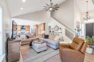 Living room featuring ceiling fan with notable chandelier, high vaulted ceiling, and light hardwood / wood-style flooring