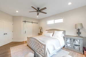 Bedroom with a barn door, light hardwood / wood-style floors, and ceiling fan