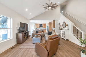 Living room with ceiling fan, a healthy amount of sunlight, light wood-type flooring, and high vaulted ceiling