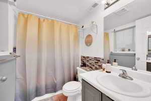 Bathroom featuring decorative backsplash, a shower with shower curtain, vanity, tile patterned flooring, and toilet