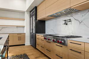 Kitchen featuring light stone countertops, stainless steel gas cooktop, tasteful backsplash, light hardwood / wood-style floors, and custom range hood