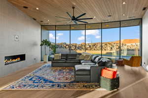 Living room with floor to ceiling windows, wood ceiling, a tiled fireplace, and light wood-type flooring