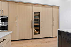 Kitchen featuring light brown cabinets, modern cabinets, light wood-type flooring, double oven, and wine cooler