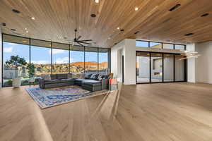 Living room with a wall of windows, a mountain view, light hardwood / wood-style floors, wood ceiling, and ceiling fan with notable chandelier