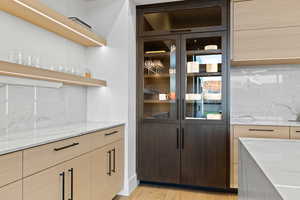 Bar area featuring decorative backsplash, beverage cooler, and light brown cabinetry