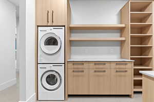 Washroom with stacked washer and clothes dryer, light tile patterned floors, and cabinet space