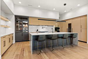 Kitchen with a breakfast bar area, light brown cabinetry, light stone counters, pendant lighting, and a kitchen island with sink