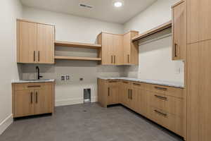 Kitchen with light stone counters, light brown cabinets, dark tile patterned flooring, and sink