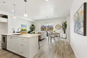 Kitchen with white cabinetry, dishwasher, sink, an island with sink, and pendant lighting