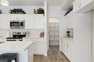 Kitchen with white cabinets, decorative light fixtures, light hardwood / wood-style floors, a kitchen bar, and stainless steel appliances