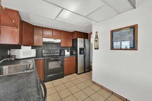 Kitchen with electric range, sink, stainless steel fridge with ice dispenser, backsplash, and light tile patterned floors