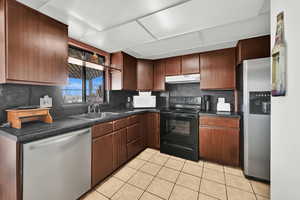 Kitchen featuring appliances with stainless steel finishes, backsplash, dark brown cabinets, sink, and light tile patterned flooring