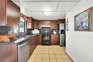 Kitchen with light tile patterned floors, backsplash, stainless steel appliances, and sink