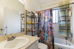 Full bathroom with lofted ceiling, vanity, shower / tub combo, and toilet