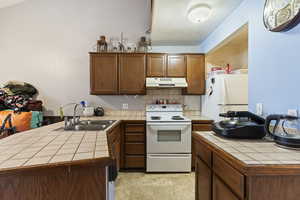 Kitchen with tile counters, decorative backsplash, white appliances, and sink