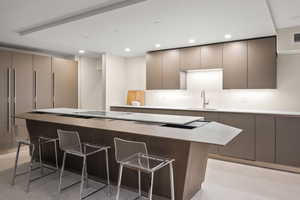 Kitchen with a breakfast bar area, a spacious island, gray cabinetry, and sink