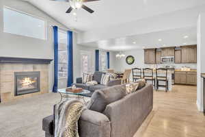 Living room with ceiling fan with notable chandelier, light hardwood / wood-style floors, lofted ceiling, and a tiled fireplace