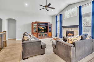 Living room featuring a tiled fireplace, ceiling fan, light hardwood / wood-style flooring, and vaulted ceiling