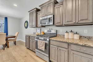 Kitchen with light stone countertops, light wood-type flooring, and appliances with stainless steel finishes