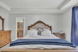 Carpeted bedroom featuring a raised ceiling and ensuite bath