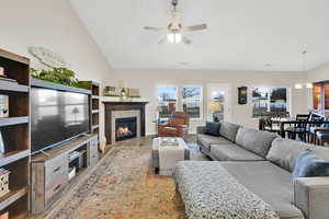 Light filled great room with large windows,a tiled fireplace, ceiling fan wood-style floors, and lofted ceiling