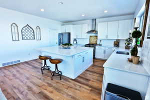 Kitchen featuring a center island, wall chimney range hood, sink, high end stainless steel range oven, and white cabinetry