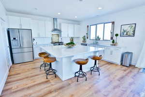 Kitchen with wall chimney exhaust hood, stainless steel fridge, a kitchen breakfast bar, and white cabinetry