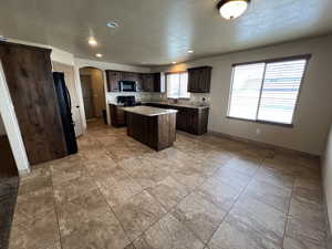 Kitchen with black appliances, light tile patterned floors, a textured ceiling, dark brown cabinets, and a kitchen island