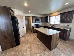 Kitchen with dark brown cabinets, a textured ceiling, sink, black appliances, and a kitchen island