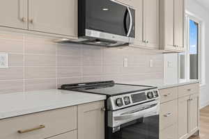 Kitchen with white cabinetry, light wood-type flooring, stainless steel appliances, and tasteful backsplash