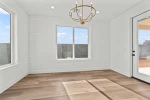 Unfurnished dining area with light hardwood / wood-style flooring, a notable chandelier, and wood walls