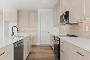 Kitchen with cream cabinets, sink, light hardwood / wood-style flooring, decorative backsplash, and stainless steel appliances