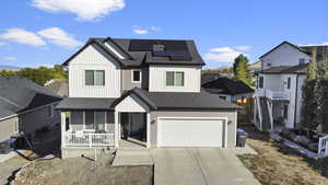 View of front of home with covered porch, a garage, and solar panels