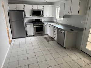 Kitchen featuring white cabinets, light tile patterned floors, sink, and appliances with stainless steel finishes