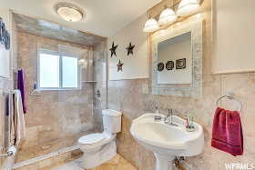 Bathroom featuring a tile shower, sink, tile walls, tile patterned flooring, and toilet