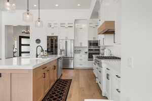 Kitchen with appliances with stainless steel finishes, extractor fan, a center island with sink, decorative light fixtures, and white cabinets