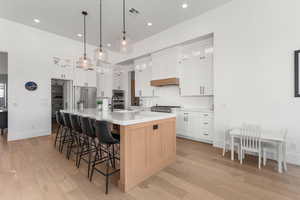 Kitchen with stainless steel appliances, sink, a center island with sink, white cabinetry, and hanging light fixtures