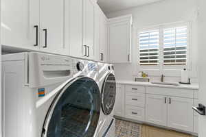 Clothes washing area with cabinets, light tile patterned floors, sink, and washing machine and clothes dryer