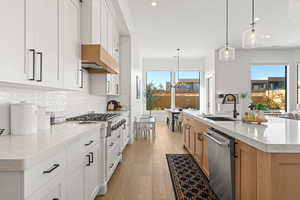 Kitchen with white cabinets, appliances with stainless steel finishes, a large island with sink, and pendant lighting