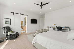 Carpeted bedroom with a barn door, ensuite bath, and ceiling fan