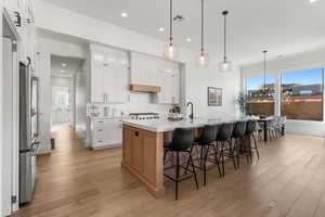 Kitchen featuring a center island with sink, stainless steel fridge, white cabinets, and pendant lighting