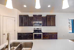 Kitchen with dark brown cabinets, sink, decorative light fixtures, and appliances with stainless steel finishes