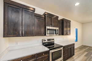 Kitchen with light hardwood / wood-style floors, dark brown cabinetry, and appliances with stainless steel finishes