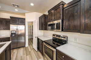 Kitchen with dark brown cabinetry, stainless steel appliances, and light hardwood / wood-style flooring