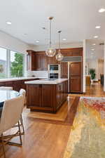 Kitchen featuring light wood-type flooring, dark brown cabinets, sink, decorative light fixtures, and a center island